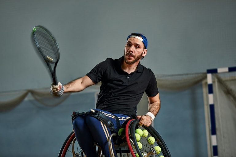 young man with a physical disability playing tennis on wheelchair on tennis court